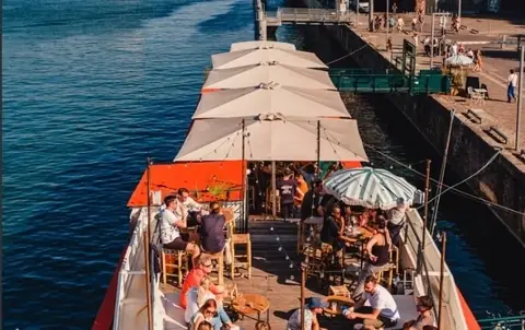 La terrasse du quai vue d'en haut, parasols et tables occupées le long de la péniche