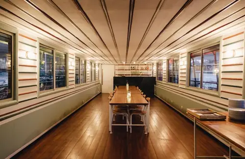 La salle restaurant vide, plafond lambrissé et grande table centrale