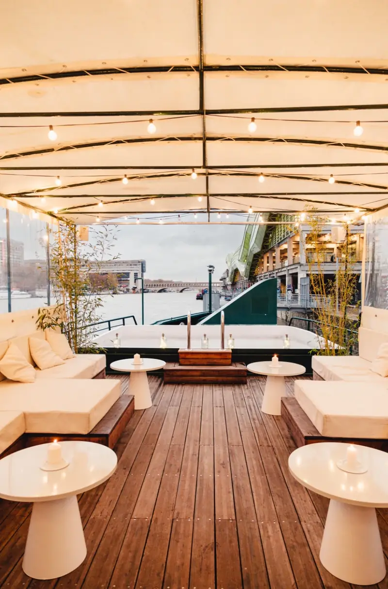 La terrasse couverte, tabourets et tables hautes face à l'ouverture sur la Seine
